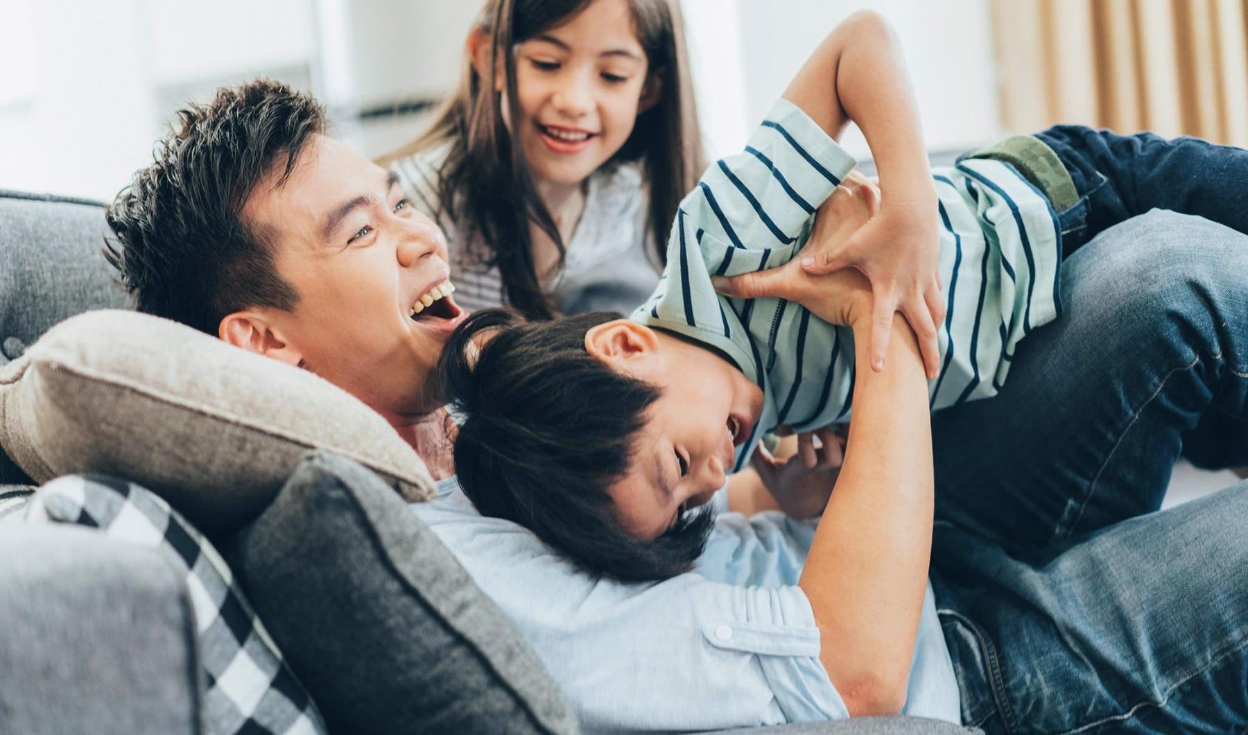 father plays on a couch with his young children